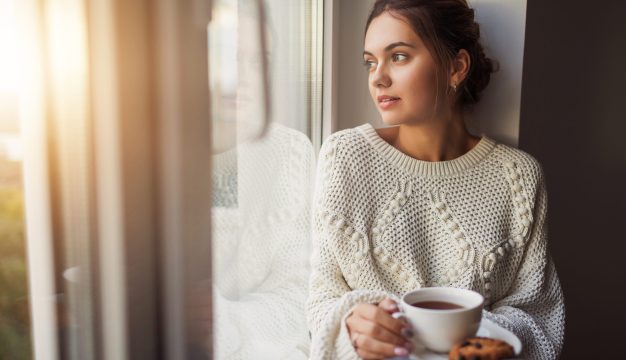 Beautiful,Young,Woman,Drinking,Coffee,And,Looking,Through,Window,While